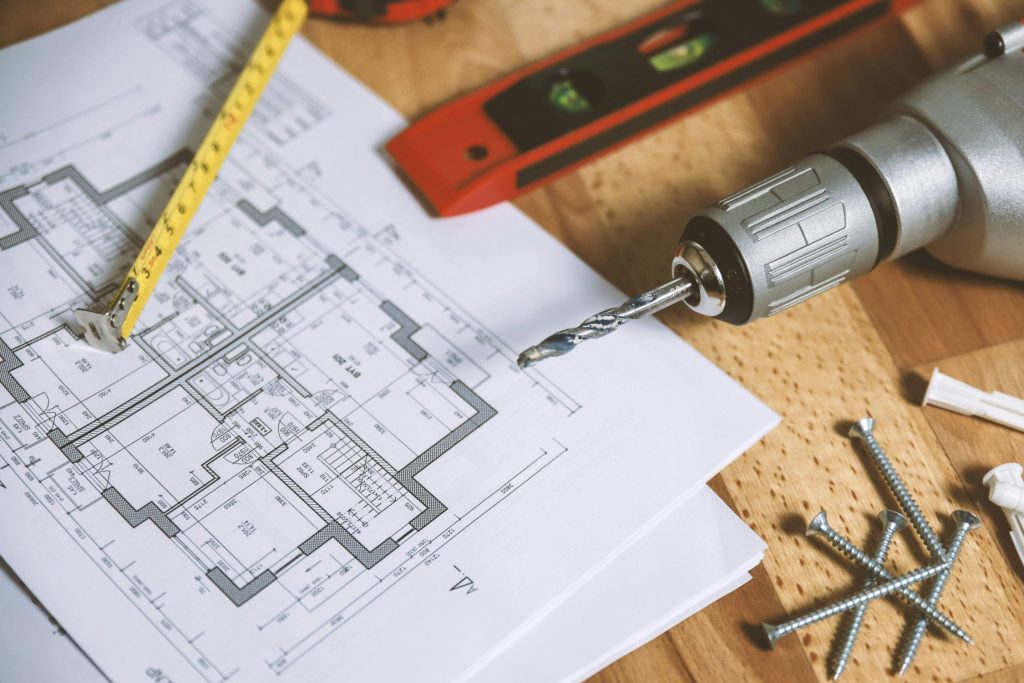 Close-up of construction blueprint with tools like drill and screws on a wooden table.